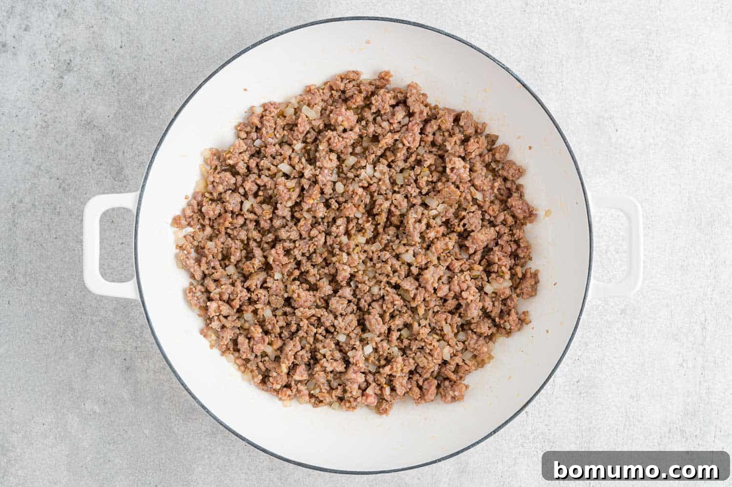 Italian sausage and diced onions browning in a large skillet.