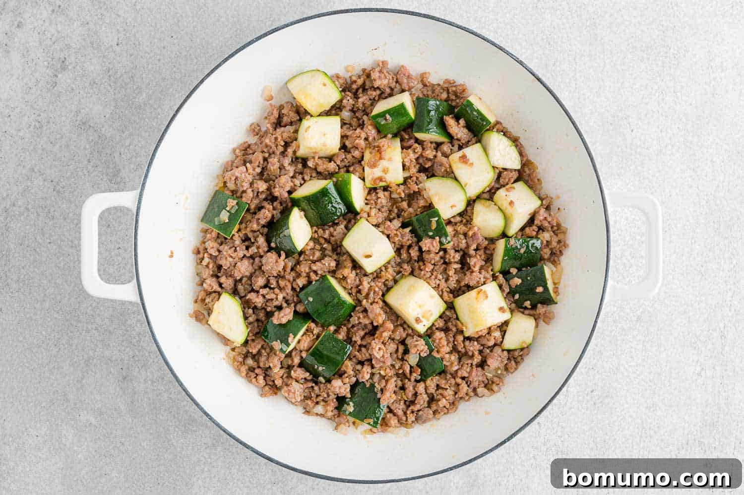 Chopped zucchini and minced garlic added to browned sausage and onions in a pan.