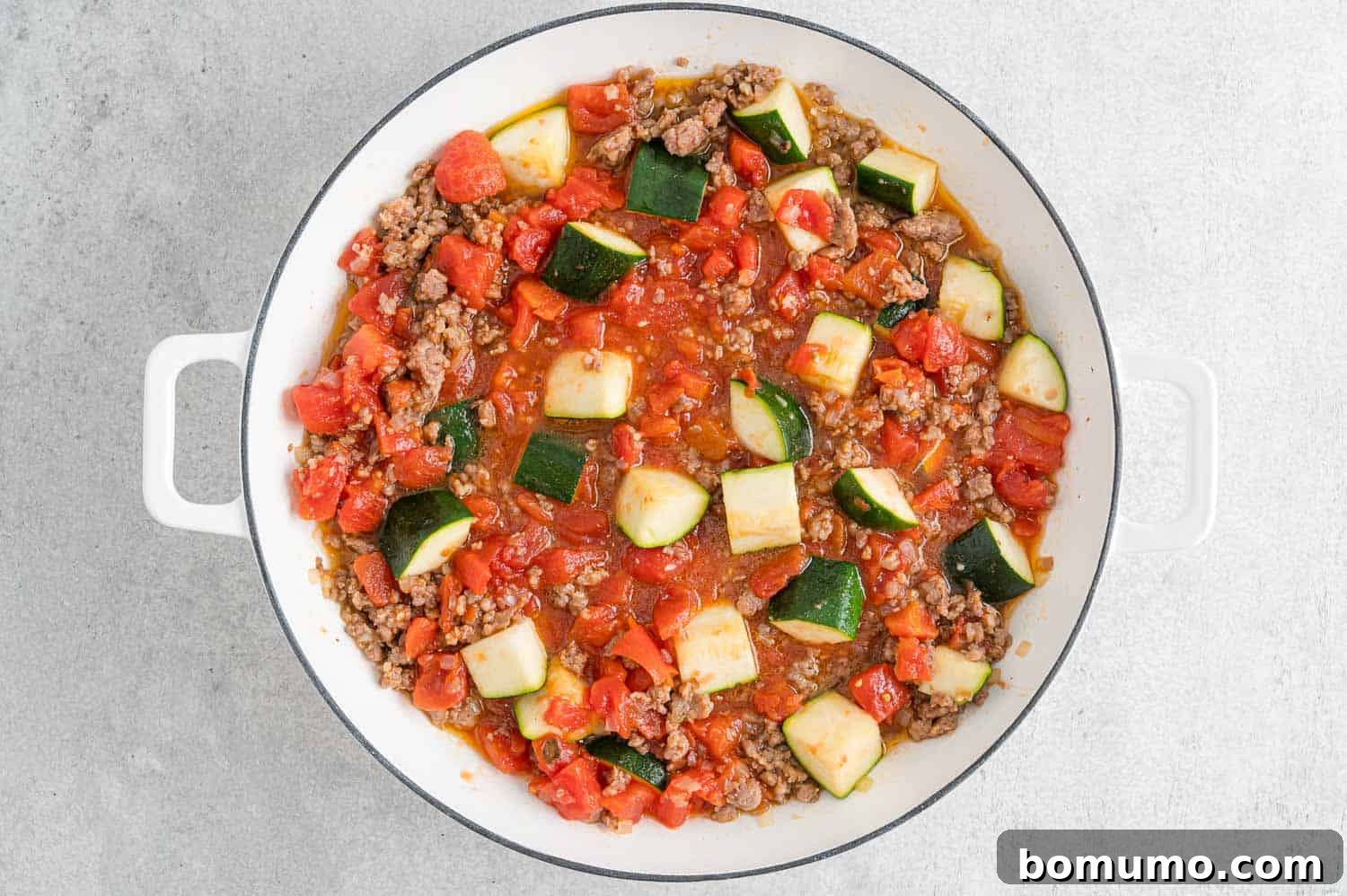 Diced tomatoes and water added to the pan, simmering to create the sauce base.