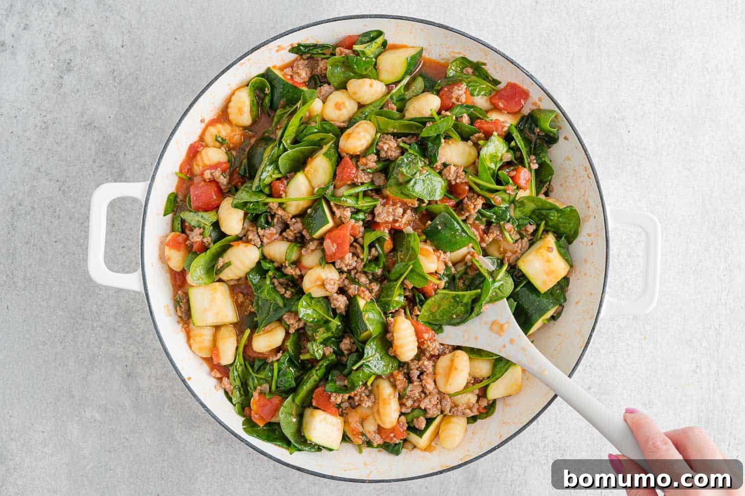 Baby spinach leaves stirred into the gnocchi and sauce mixture in the pan.
