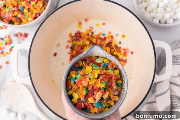 A cup of Fruity Pebbles cereal held over melted marshmallows in a saucepan.