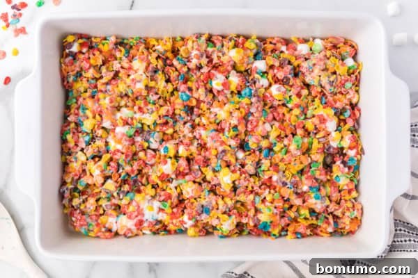 Overhead view of Fruity Pebbles treats mixture pressed into a parchment-lined baking pan.