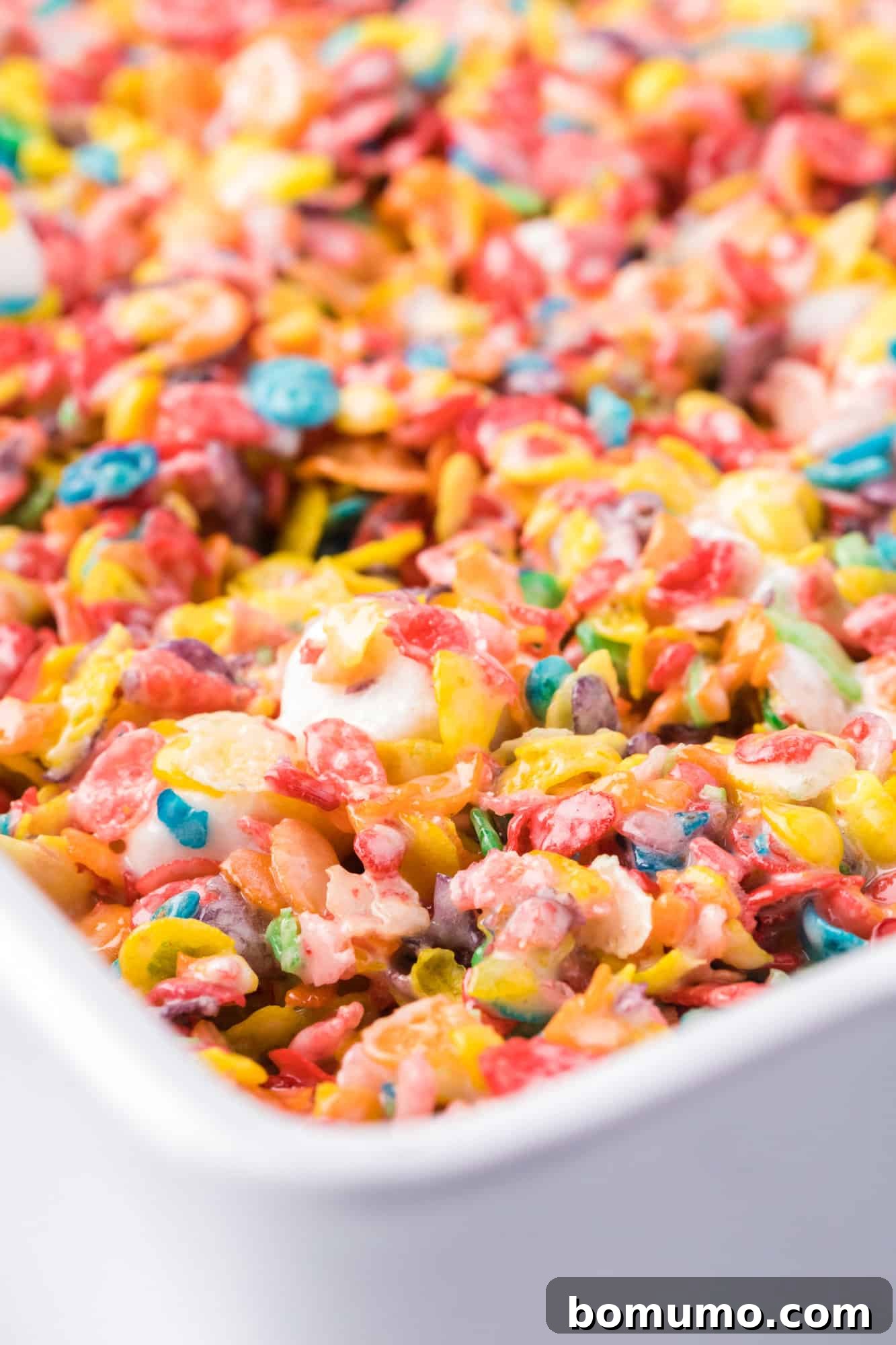 Close up of Fruity Pebbles treats in a parchment-lined baking pan.