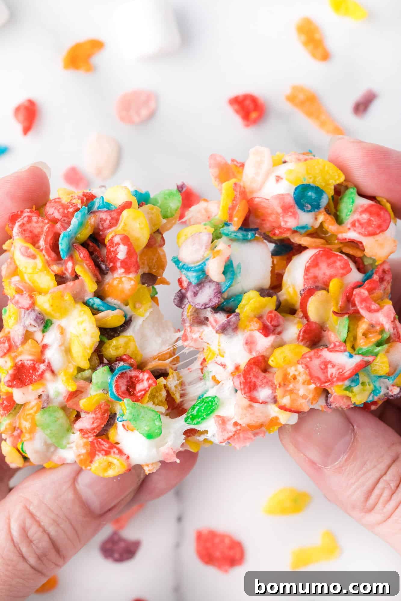 Two hands pulling apart a gooey Fruity Pebbles treat.