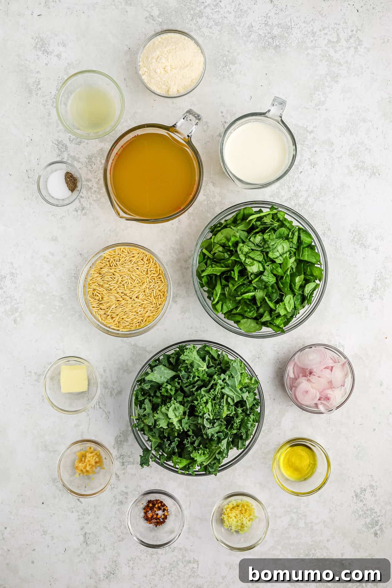Small bowls containing all the fresh ingredients needed for creamy lemon orzo: kale, spinach, orzo, cream, broth, Parmesan, lemon, and spices.