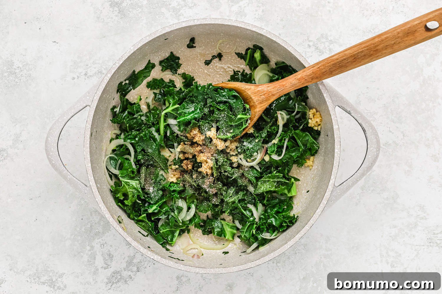 Close-up of kale being sautéed in a skillet, with garlic, salt, and pepper added, releasing aromatic steam.