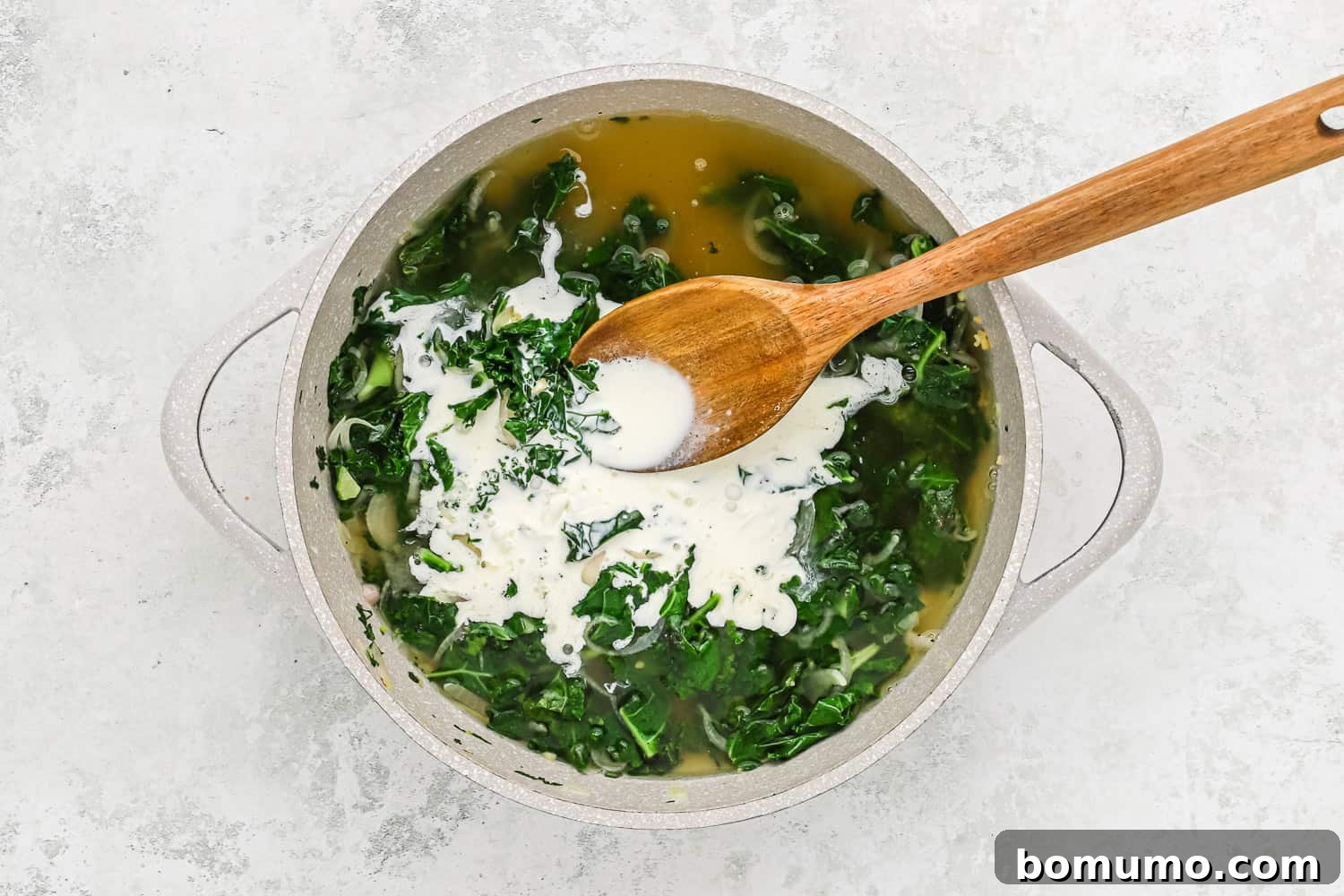Heavy cream and chicken broth being poured into the skillet with sautéed kale and shallots, creating a rich liquid base.