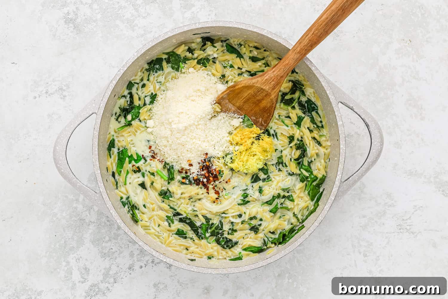 Grated Parmesan cheese and fresh lemon zest are stirred into the creamy orzo and greens, completing the dish with bright, savory flavors.