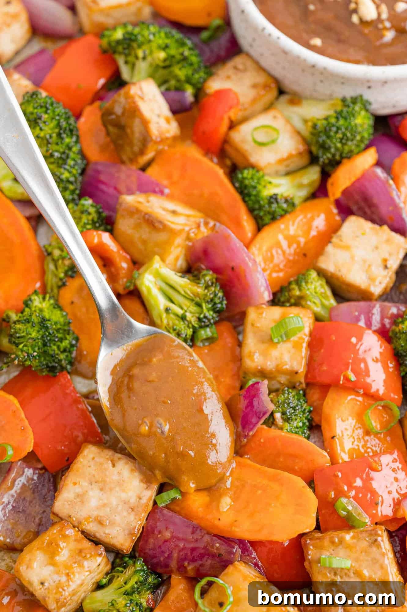 Peanut butter sauce being added to tofu sheet pan dinner, enhancing its vibrant colors and inviting texture.