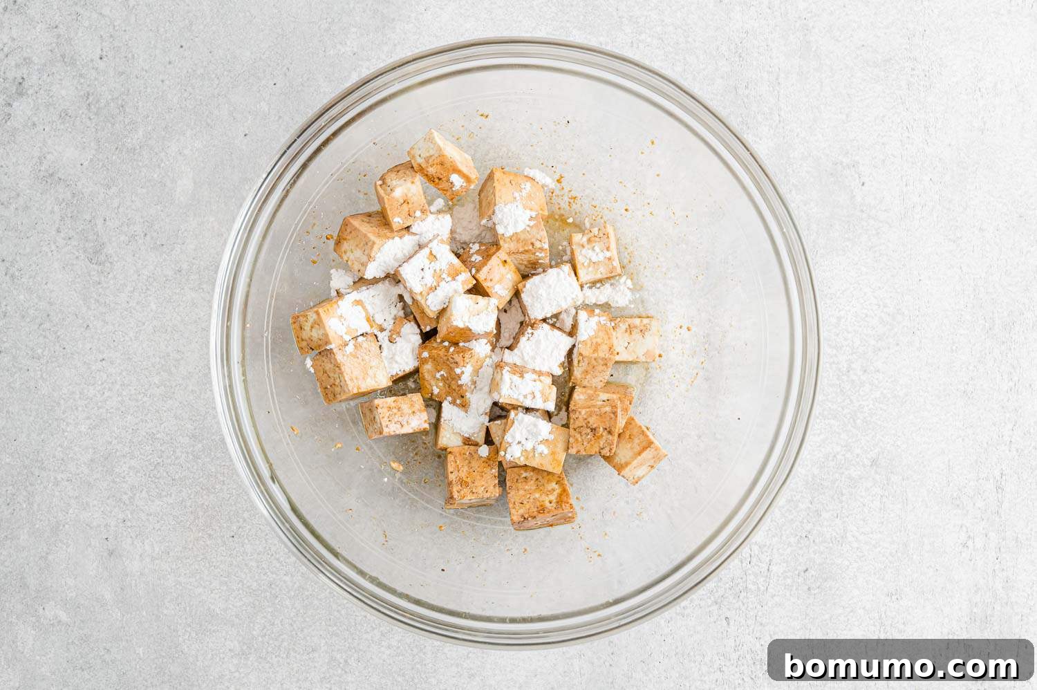 Cubed tofu, freshly seasoned with soy sauce and oil, now receiving a dusting of cornstarch to ensure extra crispiness during roasting.