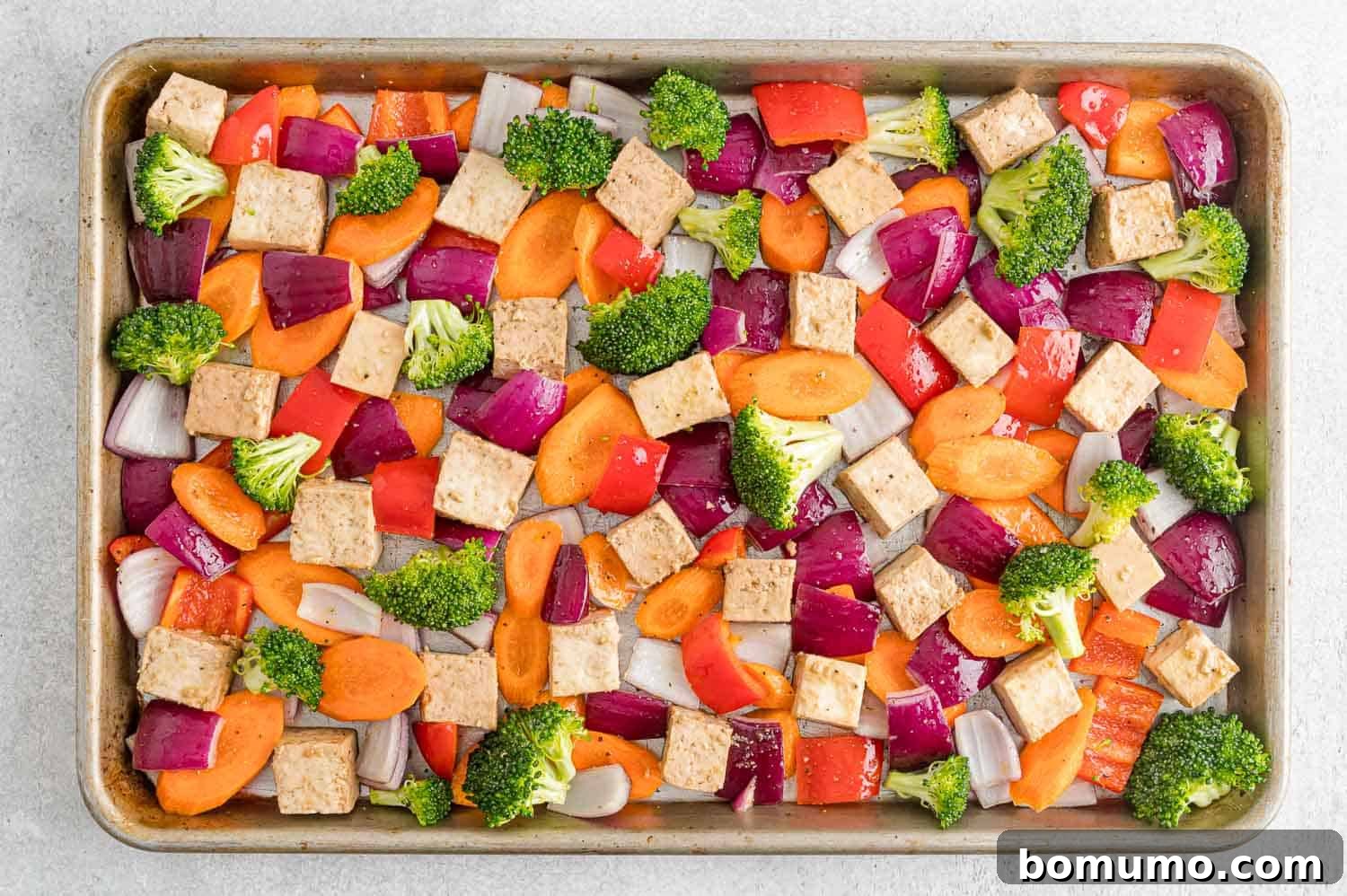 A sheet pan showcasing an organized layout of uncooked, seasoned tofu cubes alongside a vibrant mix of vegetables, perfectly arranged for roasting.