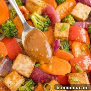 Peanut sauce being added to tofu sheet pan dinner, highlighting the appealing presentation of the meal.