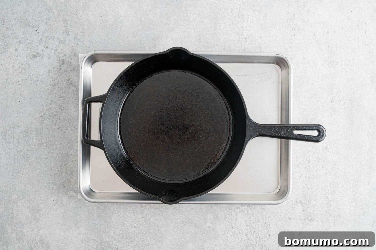 A cast iron pan placed on top of a baking sheet, effectively pressing moisture out of the tofu beneath.