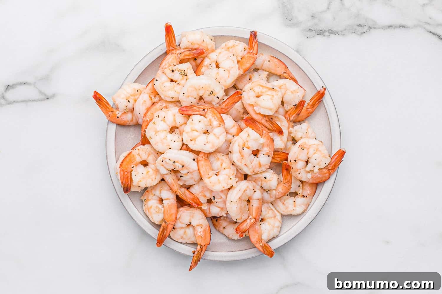 Cooked shrimp resting on a plate, plump and pink.