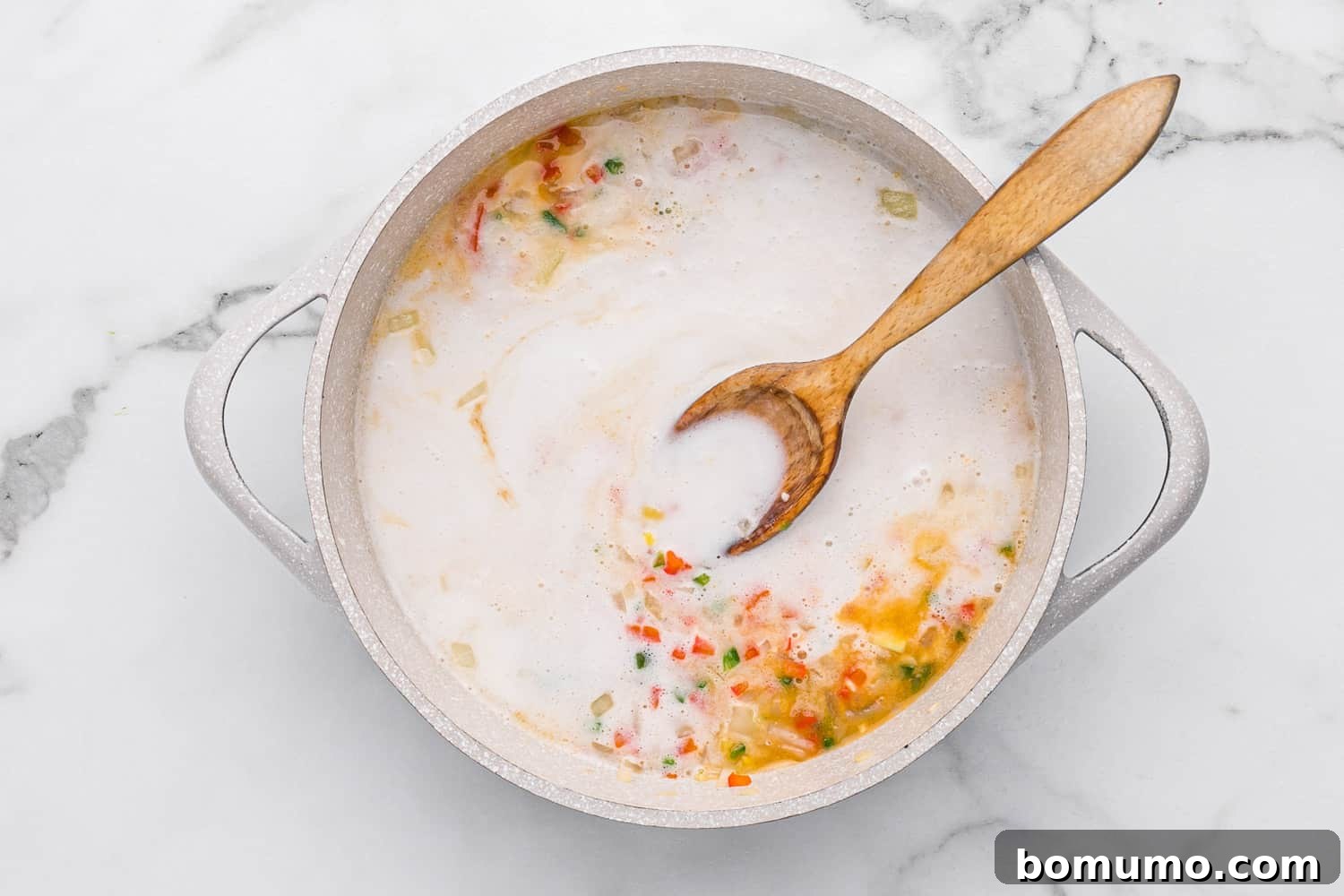 Rich coconut milk being added to the sautéed vegetables in the pan.