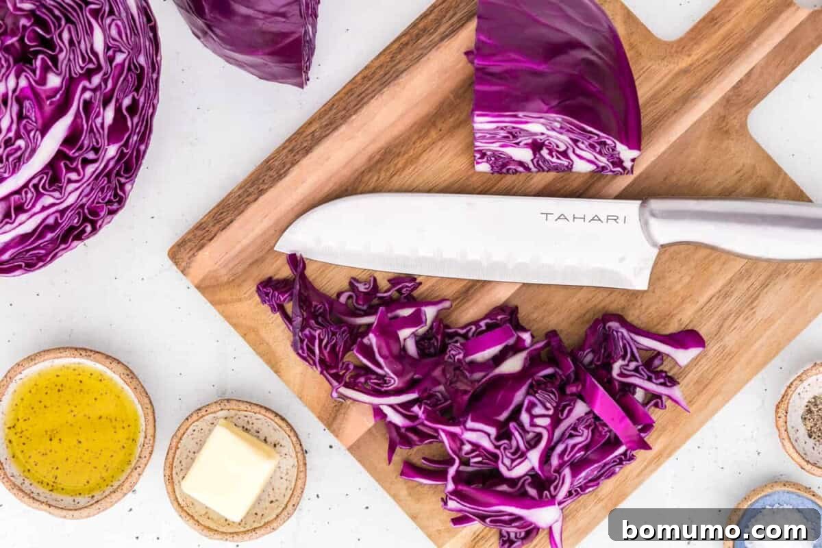 A chef's knife carefully slicing a head of red cabbage on a wooden cutting board.