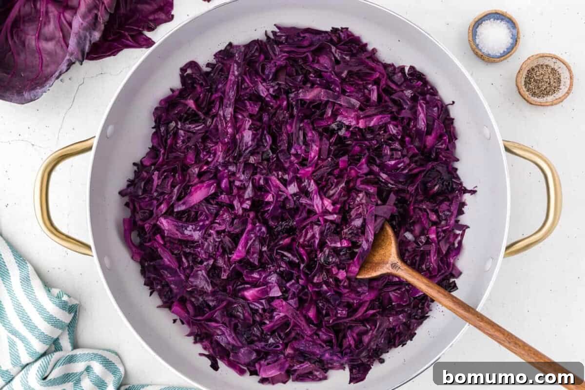 Cooked red cabbage, significantly reduced in volume and softened, simmering in a skillet.