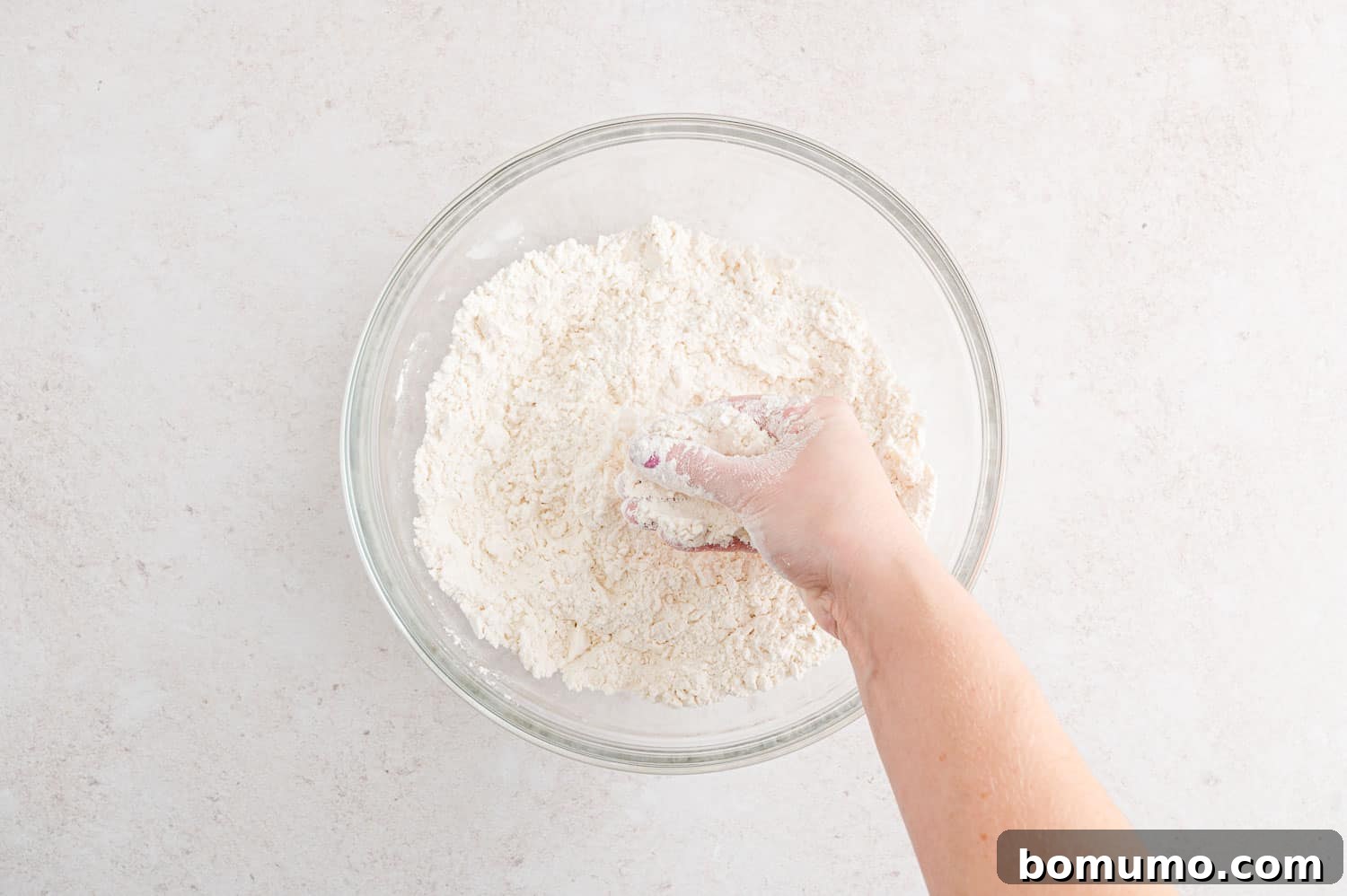 Softened butter being mixed into the flour mixture with hands.