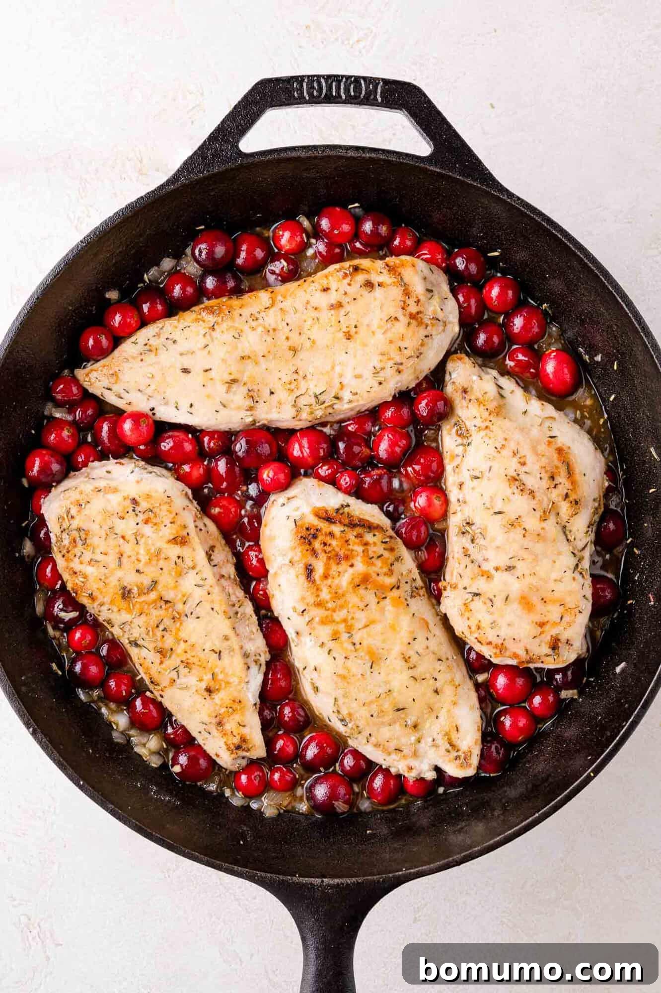 Cranberry Glazed Chicken 12 Four cooked chicken breasts with cranberries in a black cast iron skillet.
