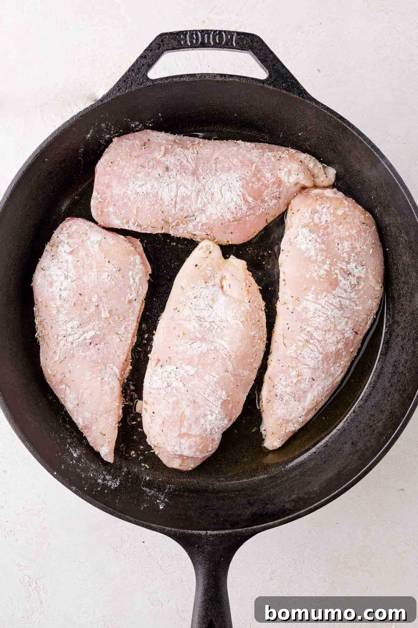 Cranberry Glazed Chicken 7 Four raw, seasoned chicken breasts in a black frying pan.