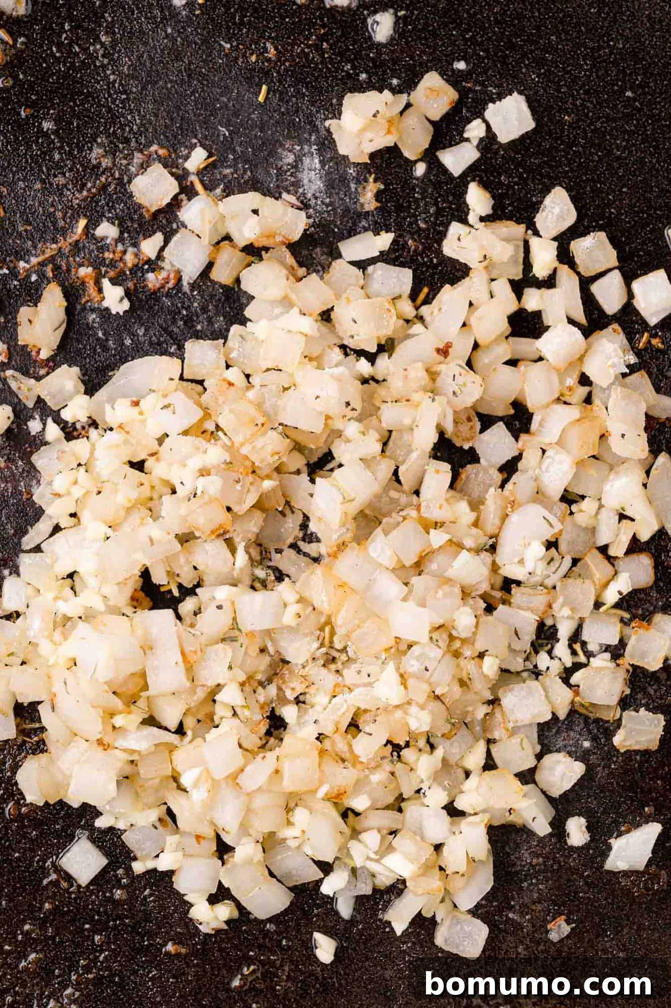 Cranberry Glazed Chicken 9 Diced onions on a dark, textured surface of a pan.