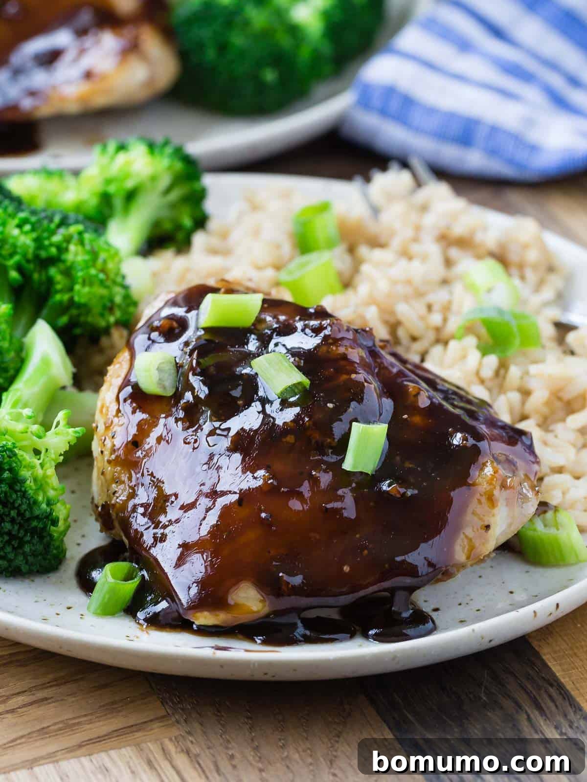 Honey balsamic chicken thigh on a plate with rice and broccoli, garnished with green onions.