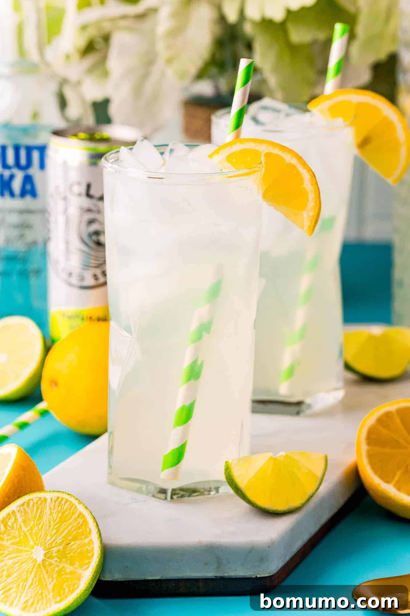Two tall glasses of zesty vodka lemonade punch with green and white straws, a can of White Claw subtly in the background.