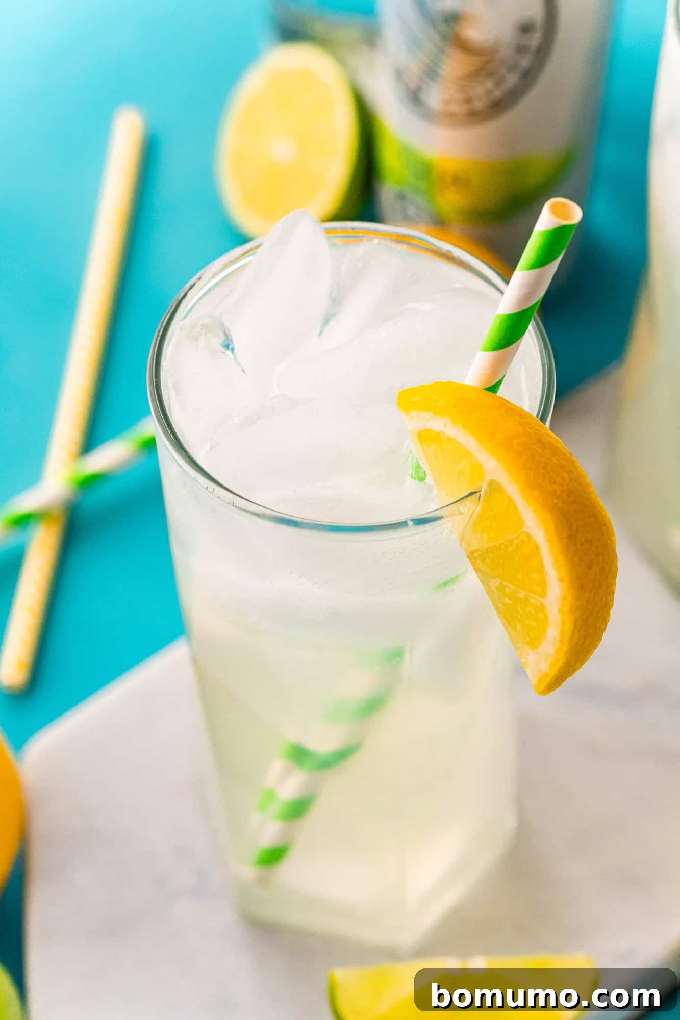 Glasses of iced beverage with a green and white paper straw and an orange wedge.