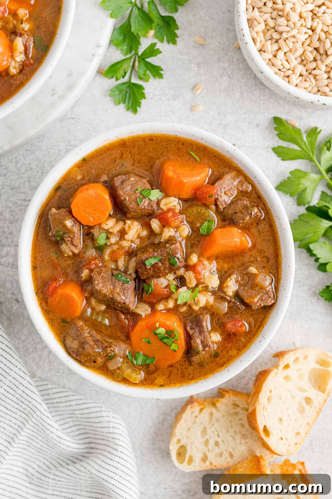 Beef barley soup surrounded by bread and parsley.