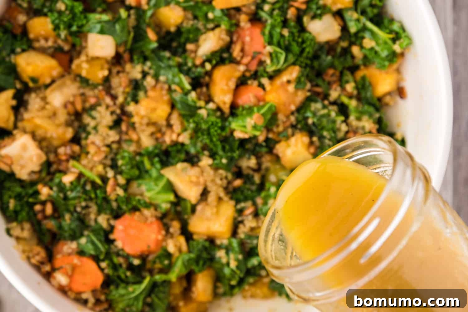 Honey mustard vinaigrette being poured over the assembled warm kale salad ingredients.