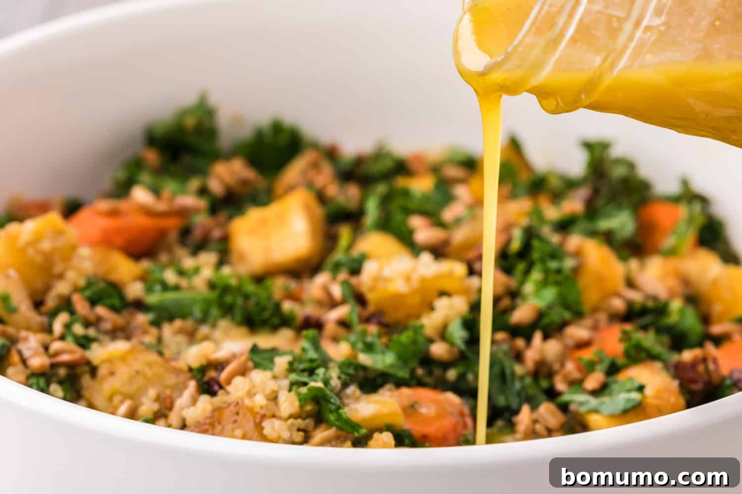The finished warm kale salad, artfully arranged on a plate with dressing poured over it.