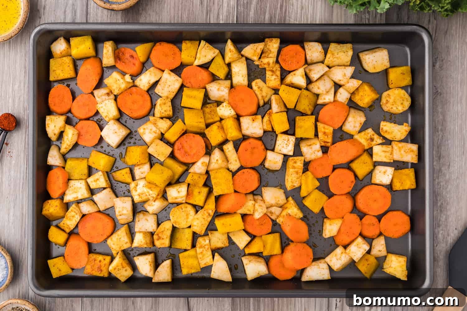 Diced root vegetables seasoned with olive oil and spices, spread on a sheet pan for roasting.
