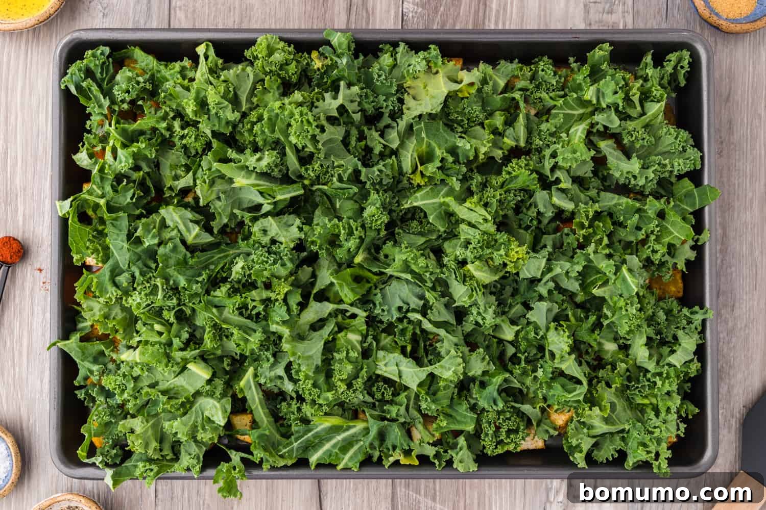 Freshly shredded kale added on top of partially roasted root vegetables on a sheet pan.
