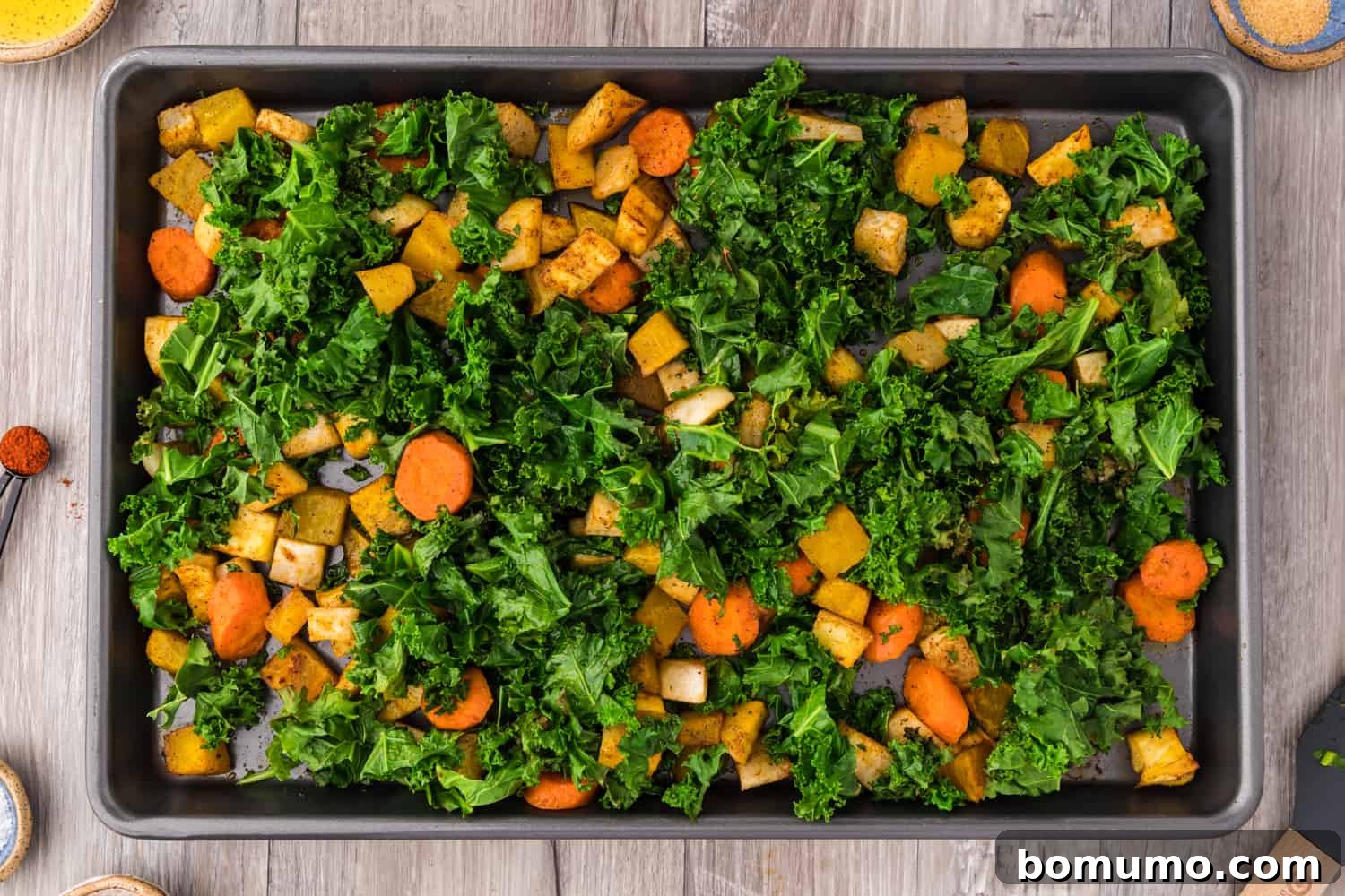 Wilted kale mixed with perfectly roasted root vegetables on a sheet pan.