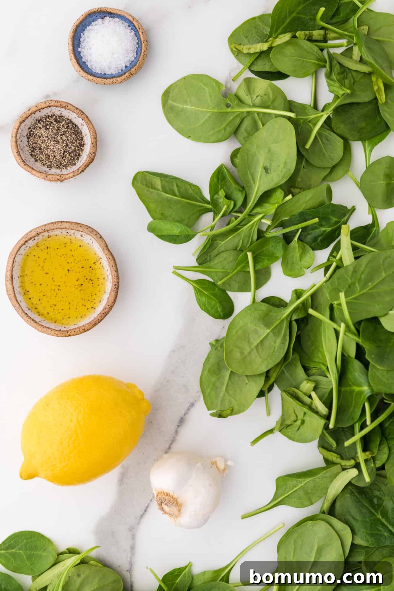 Pan-Seared Spinach Sensation 4 A collection of fresh ingredients for sautéed spinach: a bowl of vibrant spinach, a head of garlic, and a bottle of olive oil.