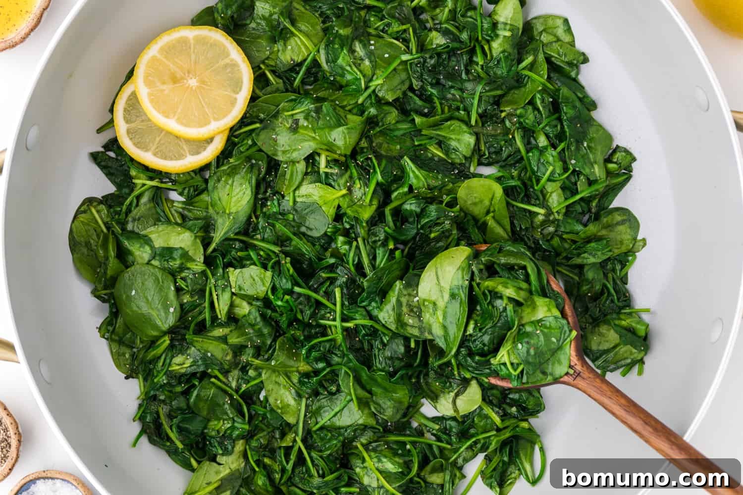 Pan-Seared Spinach Sensation 7 A bowl of freshly sautéed spinach garnished with bright lemon slices, showcasing its vibrant green color.