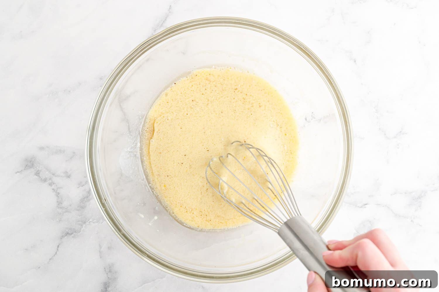 A large mixing bowl containing the wet ingredients for the muffin batter, with a whisk resting in it, showcasing a smooth mixture.