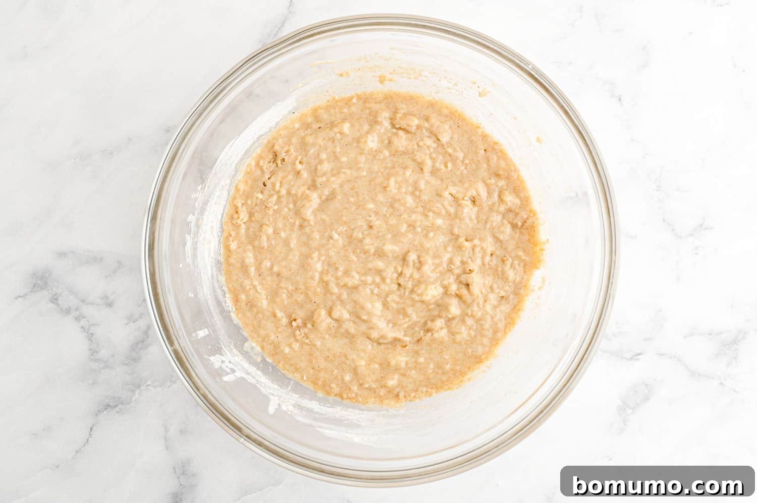 A clear glass bowl showcasing the perfectly mixed muffin batter, with a few small lumps, indicating it has not been overmixed.