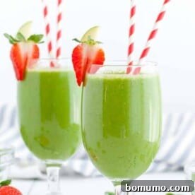 Two green drinks in stemmed glasses with red and white paper straws. Strawberries garnish the edge of the glasses.