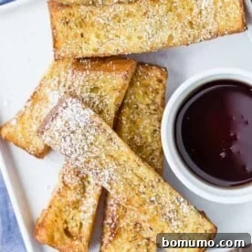 Overhead view of air fryer french toast sticks on a white plate with a bowl of maple syrup for dipping.