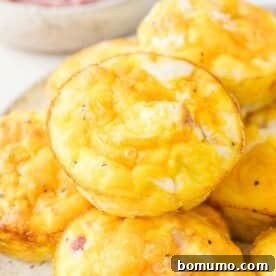 Close-up of a stack of baked egg muffins with a golden-brown top, featuring visible pieces of ham and cheese.