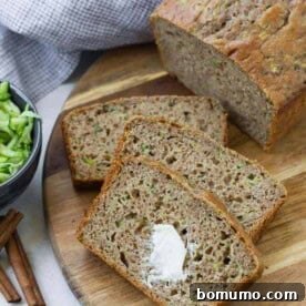 Sliced zucchini bread on a wooden surface. The top slice has a dab of butter on it.