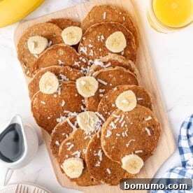 Fluffy banana coconut pancakes artfully arranged on a rustic wooden cutting board, topped with fresh banana slices and shredded coconut.