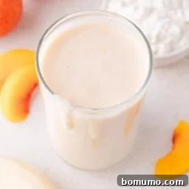 A tall glass of creamy peach cottage cheese smoothie, with fresh peach slices and a bowl of cottage cheese beside it.
