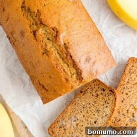 An inviting overhead shot of perfectly sliced healthy banana bread, freshly cut from a loaf on a parchment-lined cutting board, with fresh yellow bananas nearby.