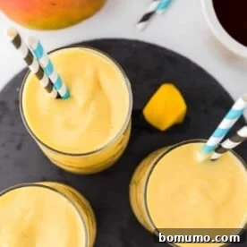 A vibrant overhead view of three refreshing mango smoothies, garnished with fresh fruit.