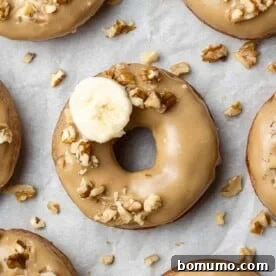 An overhead shot of a glazed baked banana donut, garnished with crunchy walnuts and a fresh banana slice.
