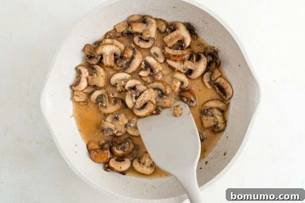 A spatula stirs sautéed mushrooms as Marsala wine is poured into the skillet, deglazing the pan.