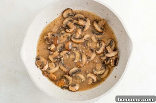 Sautéed mushrooms simmering in a rich Marsala wine and broth mixture in a skillet.