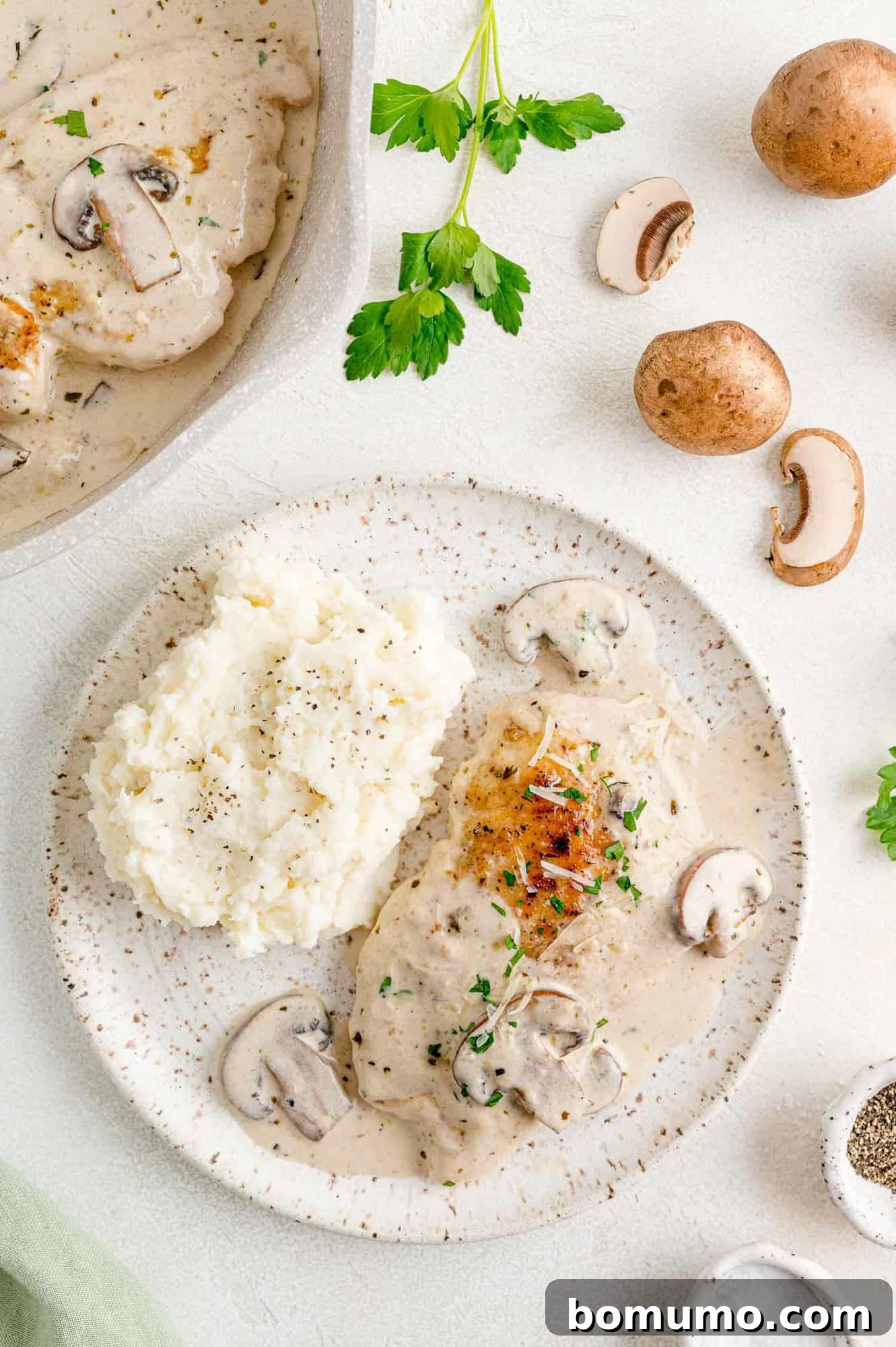 A beautifully plated serving of chicken marsala on a white dish, accompanied by sautéed mushrooms and creamy mashed potatoes.